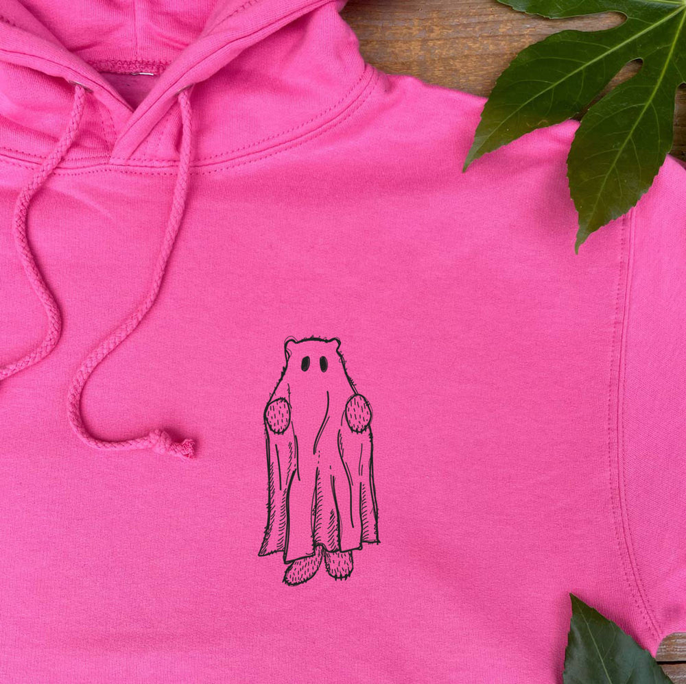 Pink hoodie with a ghost design on a wooden surface with leaves.