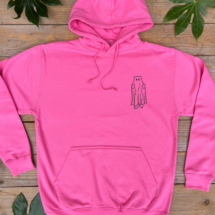Pink hoodie with a small graphic on a wooden surface with leaves.