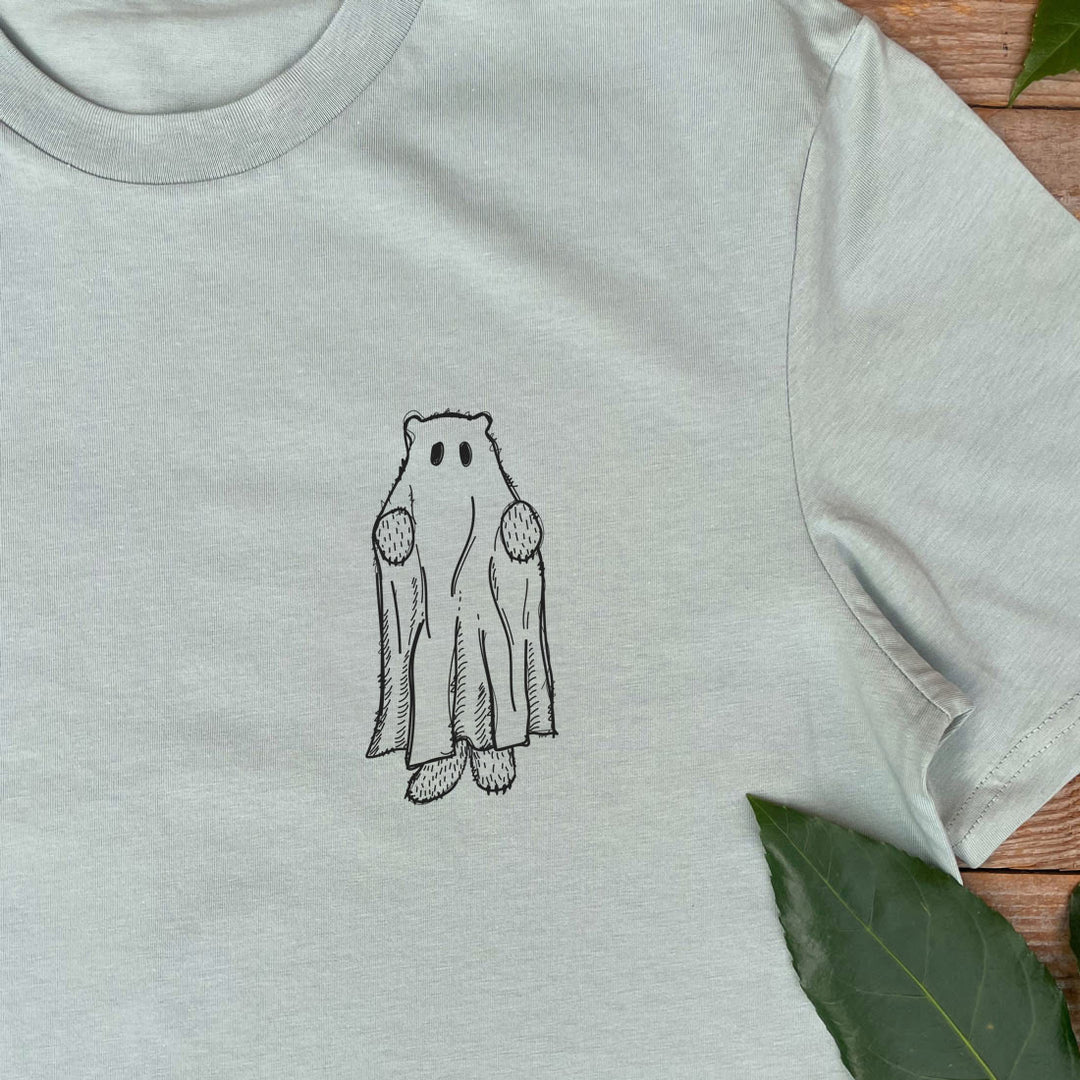 Light gray t-shirt with a black outline of a ghost design on a wooden surface with leaves.