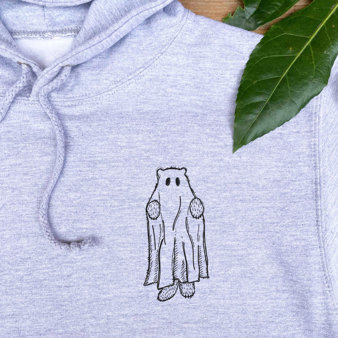 Light blue hoodie with a black and white embroidered design of a ghost wearing a cape on a wooden surface with leaves.