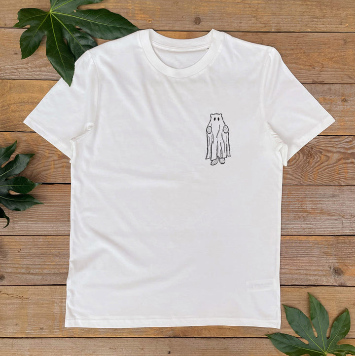 White t-shirt with a small owl design on a wooden surface with leaves.