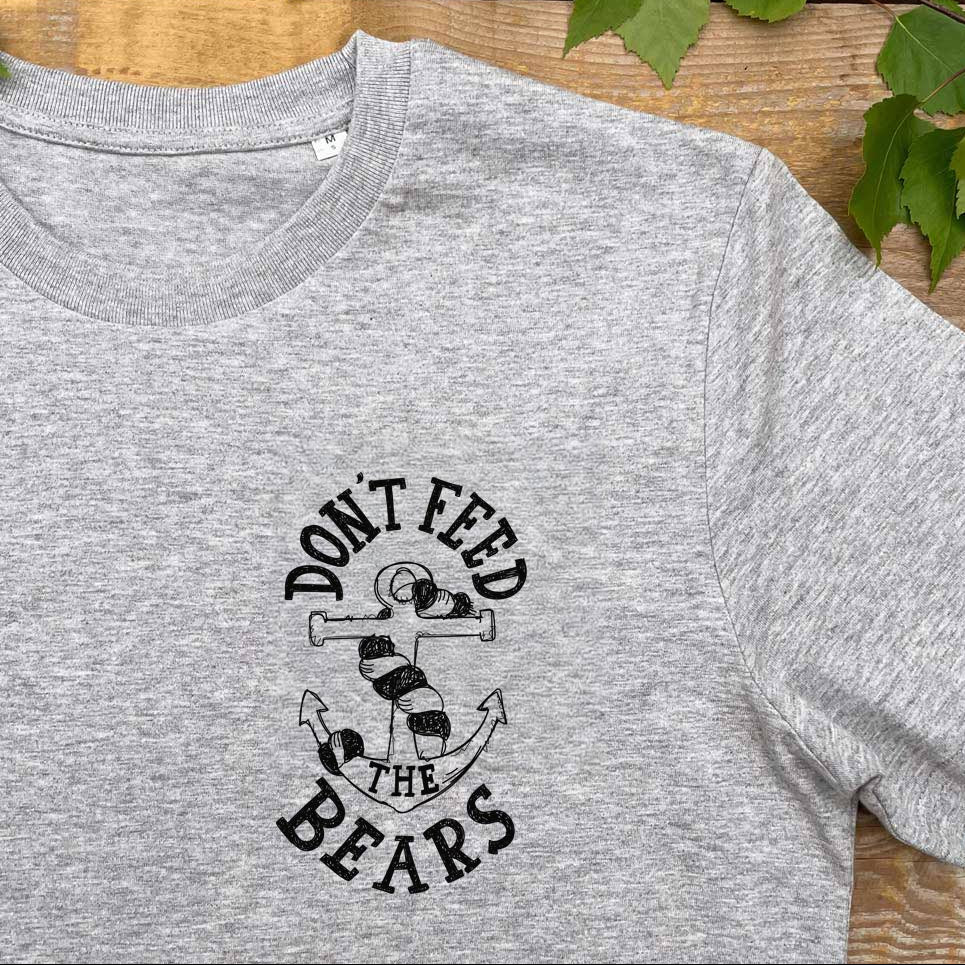 Gray t-shirt with 'Don't Feed the Bears' graphic on a wooden surface with leaves.