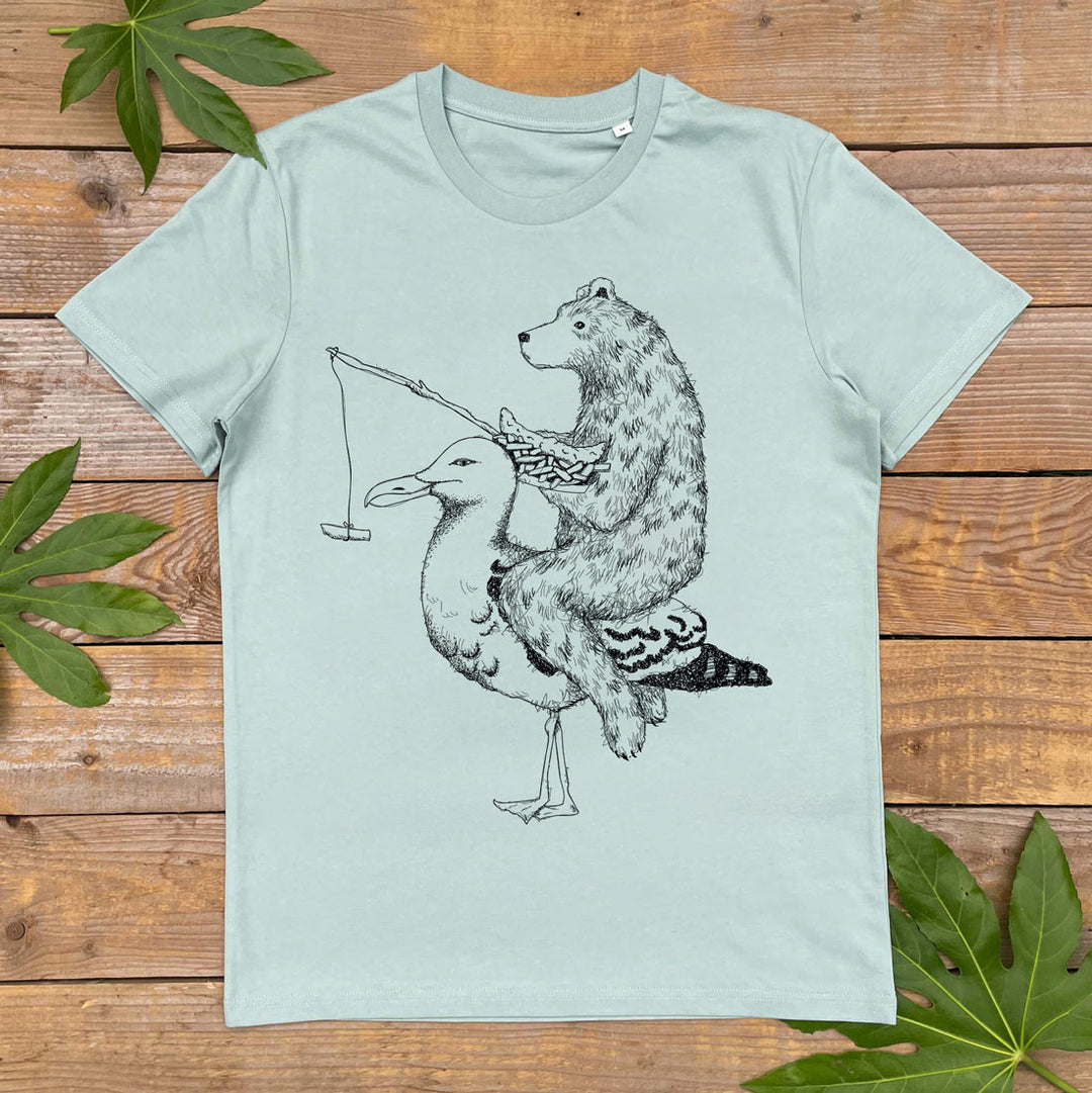 Light blue t-shirt with a graphic of a bear riding a seagull on a wooden background