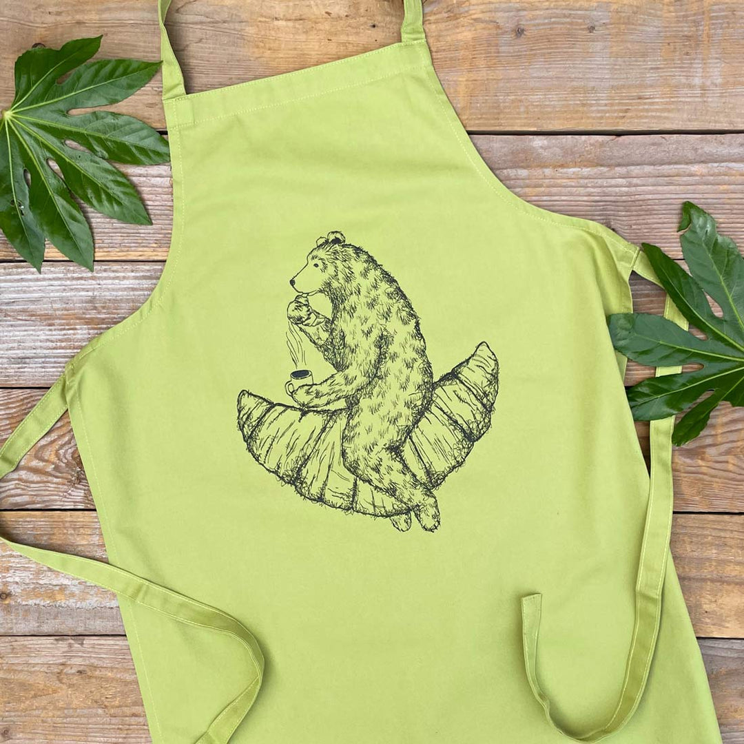 green apron with a bear sat on a croissant design