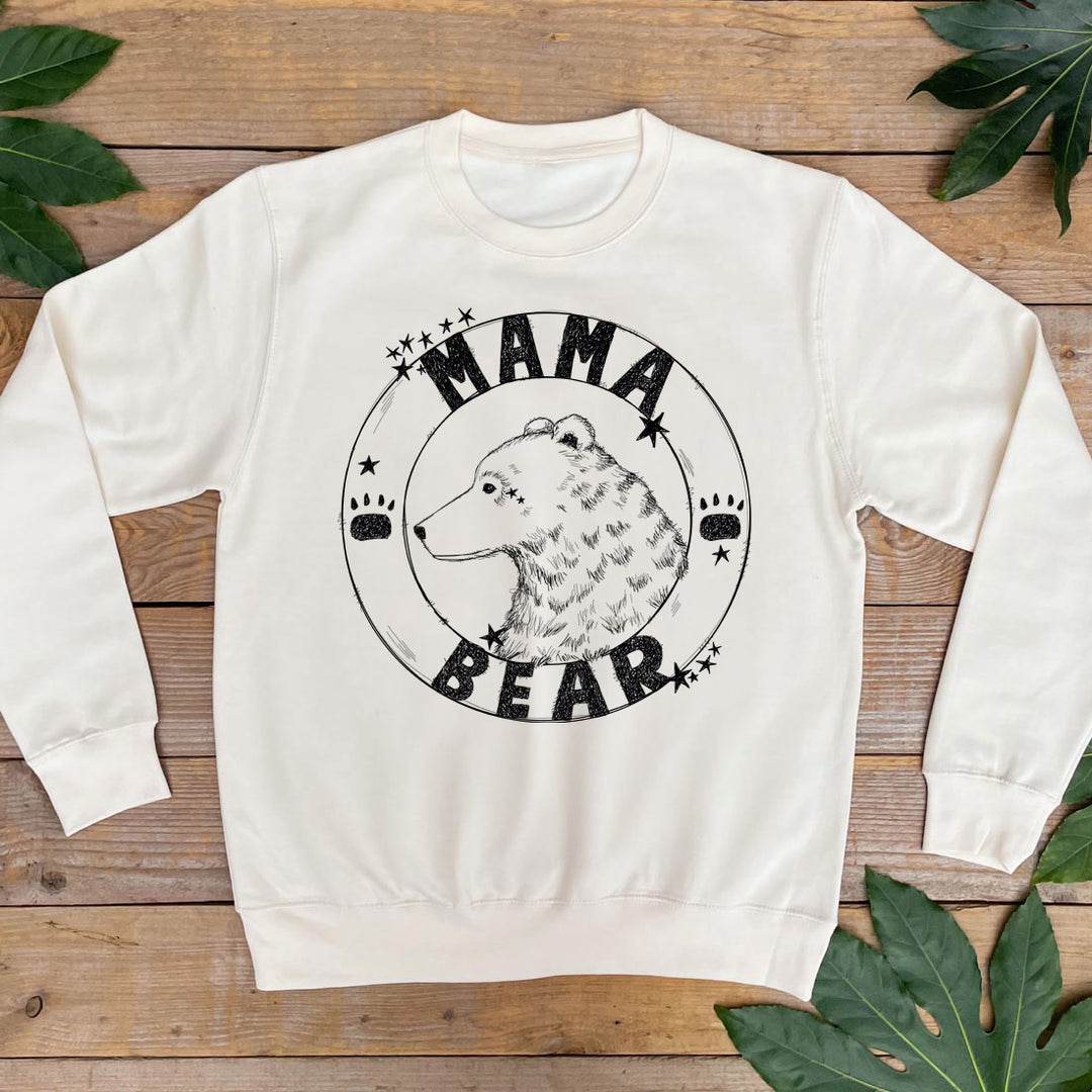 White sweatshirt with 'Mama Bear' graphic on a wooden surface with leaves.