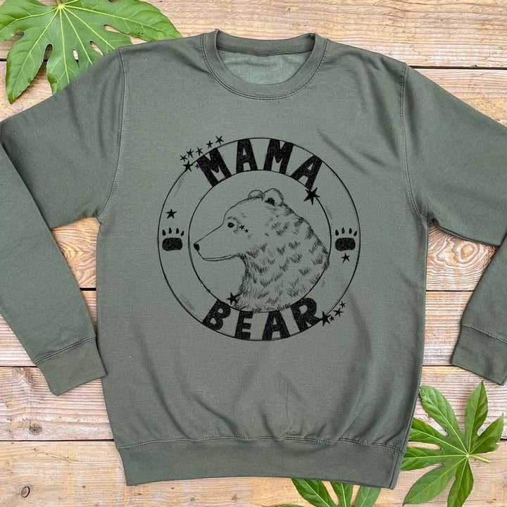 Green sweatshirt with 'Mama Bear' graphic on a wooden surface with leaves.